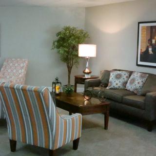 A cozy living room with a sofa, armchair, and a coffee table, complemented by a lamp and decorative elements.