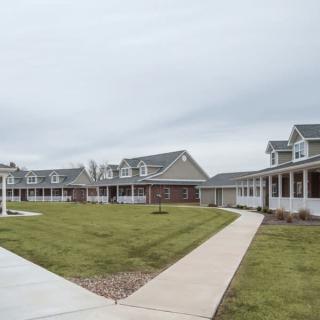 A residential area with multiple houses, a green lawn, and a paved walkway under an overcast sky.