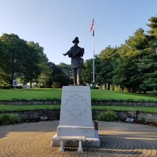 A statue standing tall in a serene park setting, complemented by an accompanying flag.
