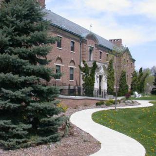 A pathway leads to a large brick building surrounded by trees and greenery.