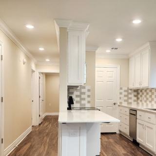 A modern kitchen with white cabinetry, wood flooring, and recessed lighting.
