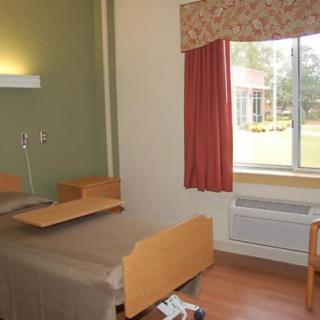 A hospital room featuring a single patient bed with an adjacent window and simple furnishings.