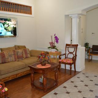 A cozy living room with a comfortable sofa, armchair, and a wooden coffee table. A television is mounted on the wall, and an orchid adds a touch of elegance to the decor.