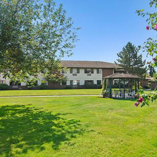 A lush green lawn with a gazebo and a building in the background on a sunny day.