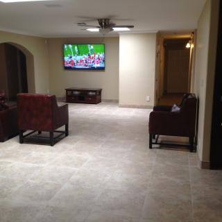 A spacious living room with tile flooring, featuring a wall-mounted television and comfortable seating.