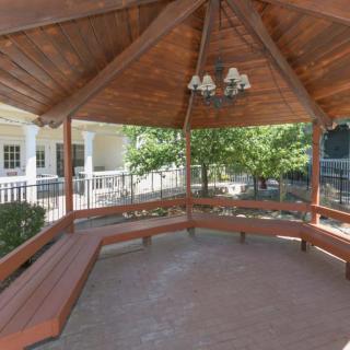 A wooden gazebo with built-in benches, surrounded by a garden setting.