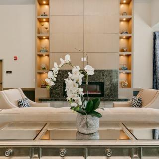 A modern living room featuring a central fireplace, elegant furniture, and a potted orchid on a glass coffee table.