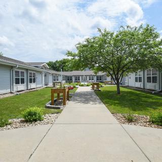 A peaceful courtyard surrounded by buildings with a pathway, benches, and lush greenery under a cloudy sky.