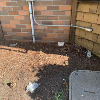 A brick wall with an electrical conduit and scattered debris on the ground.