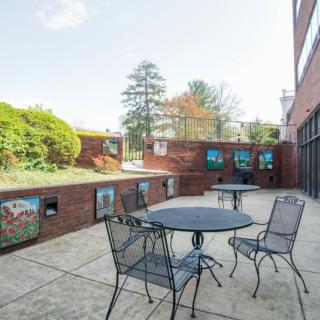 A sunny outdoor patio area with metal tables and chairs, surrounded by a brick wall decorated with colorful artwork.