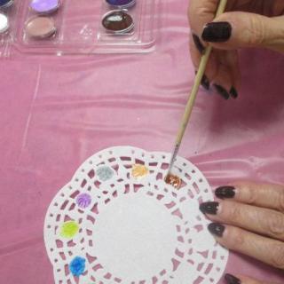 A person painting a decorative doily with watercolors.