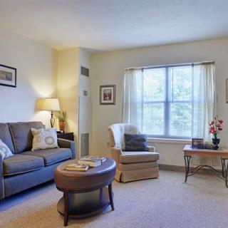 A cozy living room with a sofa, armchair, and coffee table by a window with curtains.