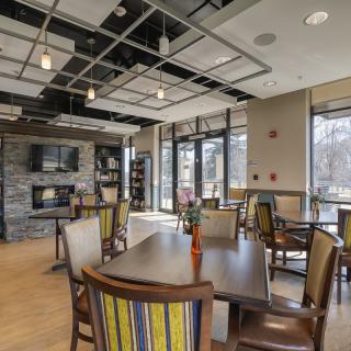 A modern dining area with tables, chairs, and a fireplace, illuminated by natural light.