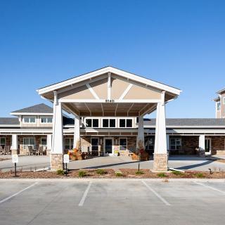 A modern building with a prominent entrance and spacious parking area under a clear blue sky.