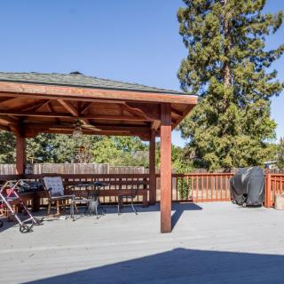 A spacious backyard deck with a wooden pergola, outdoor furniture, and a grill under a clear blue sky.