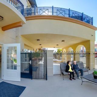 A sunny outdoor patio with seating and people near a building entrance.