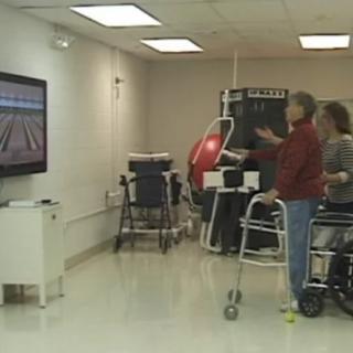 An elderly person engages in a virtual bowling game as part of a rehabilitation session in a healthcare facility.