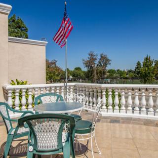 A sunny outdoor patio with a table and chairs, overlooking a scenic view with an American flag waving against the clear blue sky.
