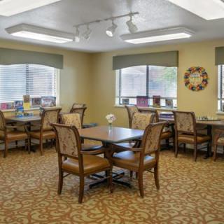 A well-lit dining area with several tables and chairs, featuring large windows and decorative elements.