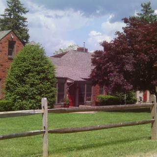 A suburban house with a wooden fence, surrounded by trees and a well-kept yard.