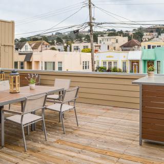 A spacious rooftop deck with a table and chairs, overlooking an urban neighborhood.