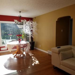 A cozy living and dining area featuring a round table with chairs, a chandelier, a couch, and large windows allowing natural sunlight to brighten the space.