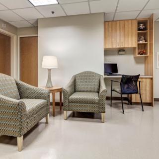 A cozy waiting area featuring two patterned chairs, a lamp, and a desk setup.