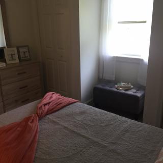 A cozy bedroom with a bed, dresser, and window letting in natural light.