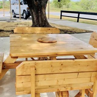 A wooden picnic table with benches under a tree in an outdoor setting.
