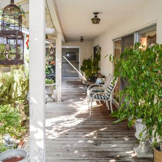 A cozy porch with abundant greenery, featuring wooden flooring and outdoor seating.