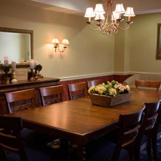 A dining room with a wooden table and chairs, featuring a floral centerpiece and chandelier lighting.