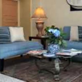 A cozy living room with blue sofas, a coffee table adorned with flowers, and a warm lamp.