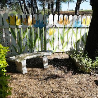 A peaceful garden spot featuring a stone bench and a beautifully painted fence.