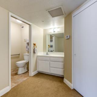 A small bathroom with a toilet and vanity sink, featuring a wall mirror and bright lighting.