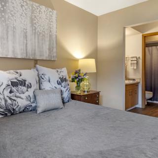 A cozy bedroom with modern decor featuring a bed, nightstand with a lamp, and an adjoining bathroom.