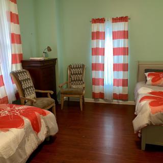 A cozy bedroom with light green walls, featuring a bed, two chairs, a dresser, and red-and-white striped curtains.