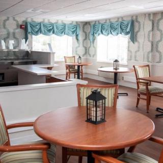 A cozy dining area with round tables and wooden chairs, decorated with lantern centerpieces and patterned curtains by the windows.