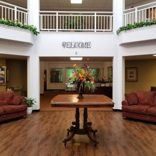 A welcoming lobby area featuring a central table with floral arrangement, surrounded by comfortable sofas and decorative plants.