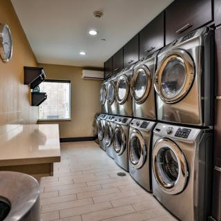 A modern laundry room featuring multiple washing machines and dryers lined up against the wall.