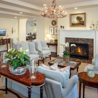 A cozy living room with a traditional design featuring a fireplace, chandelier, and elegant seating arrangement.
