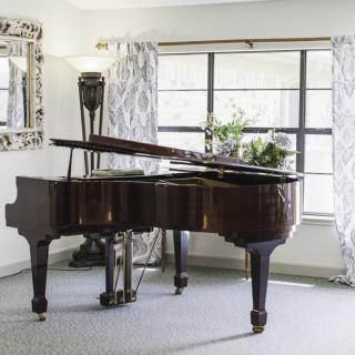 A grand piano elegantly positioned in a well-lit room with large windows and decorative curtains.