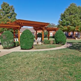 A beautifully landscaped garden with a wooden pergola, trimmed bushes, and a winding pathway.