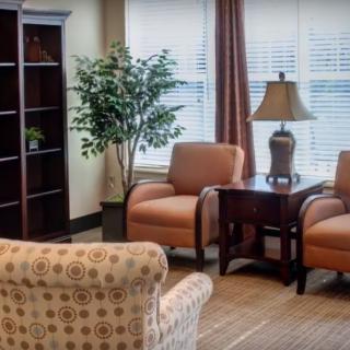 A cozy living room with two armchairs, a side table holding a lamp, and a bookshelf in the corner.