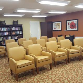 A waiting room with rows of beige chairs and a bookshelf in the background.