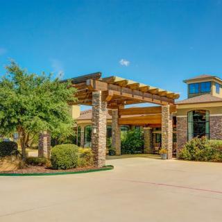 A sunny day view of a building entrance with a landscaped driveway.