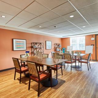 A spacious meeting room with tables and chairs, featuring wooden flooring and art on the walls.