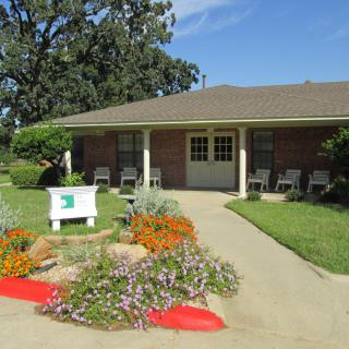 A charming brick building with a landscaped garden and outdoor seating on a sunny day.