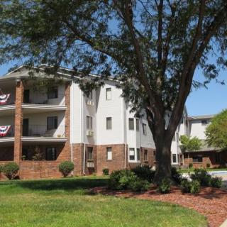 A residential apartment building with balconies, surrounded by well-maintained landscaping and a large tree.
