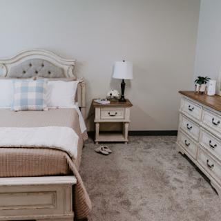 A cozy and elegantly designed bedroom featuring a comfortable bed, stylish nightstand with lamp, and a spacious dresser.