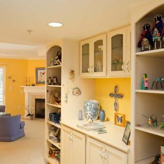 A cozy living room with yellow walls, featuring storage shelves filled with various decorations and a fireplace.